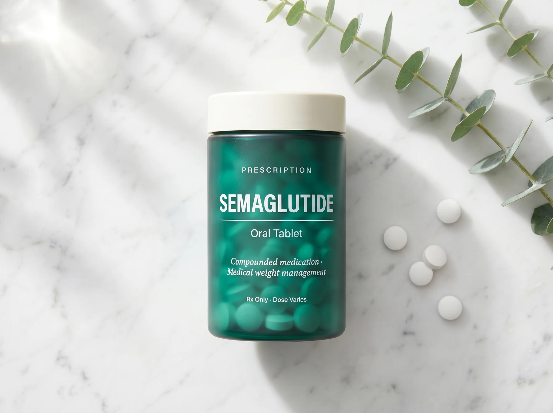 REMEVi compounded oral semaglutide in a deep teal translucent prescription bottle with cream cap, on cream marble with scattered white tablets and fresh eucalyptus